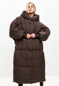 Smeđa podložena jakna s visokim ovratnikom, oversize dizajnom i elastičnim manžetama. Ima bočne džepove i četvrtasti uzorak.