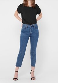 T-shirt nero a maniche corte abbinato a jeans blu a vita alta. I jeans hanno una vestibilità slim e un orlo alla caviglia. Tacchi neri con cinturini completano l'outfit.