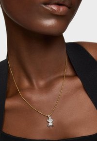 Collana in oro con pendente a forma di orsetto in argento, caratterizzata da una finitura liscia. Indossata su un tessuto scuro, esalta il design della gioielleria.