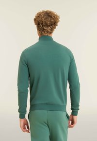 Felpa verde con zip realizzata in tessuto morbido. Presenta un collo alto, maniche lunghe e polsini e orlo a costine. Texture liscia senza motivi.