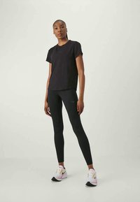 Μαύρη βαμβακερή μπλούζα με κοντό μανίκι, συνδυασμένη με μαύρες κολάν. Λευκά και ροζ αθλητικά παπούτσια με αντιθέτοντα μαύρα στοιχεία.