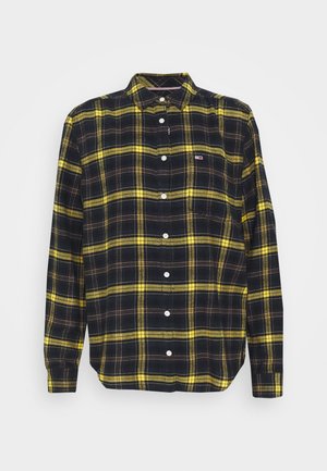 Chemise noire à manches longues boutonnée avec motif à carreaux jaunes et petit logo sur la poche poitrine gauche, présentée sur fond blanc.