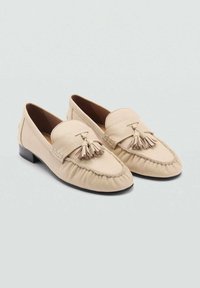 Beige läderloafers med fransar, med en rund tå och veckad detaljer. Låg svart klack, slät textur och minimalistisk design.