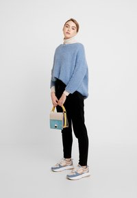 Lyseblå fluffy sweater, sorte fløjl bukser og multicolor sneakers. Bærer en lille håndtaske i lyseblå, beige og gul.