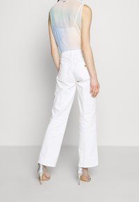 Pantaloni bianchi a gamba larga con vita alta e due tasche posteriori. Abbinati a scarpe con tacco alto argentate. Modello mostrato di spalle.