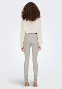 Jeans fitted grigio chiaro abbinati a un maglione in maglia color crema, caratterizzati da una silhouette rilassata e un tessuto testurizzato. I tacchi completano l'outfit.