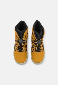 Bottes avec un dessus synthétique texturé jaune et noir, présentant un design à lacets et un intérieur rembourré pour la chaleur et le confort.