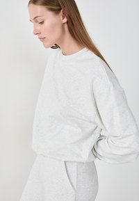 Hellgrauer Sweatshirt aus weichem, strukturiertem Stoff mit Rundhalsausschnitt und heruntergesetzten Schultern, in lockerer Passform und minimalistischem Design.