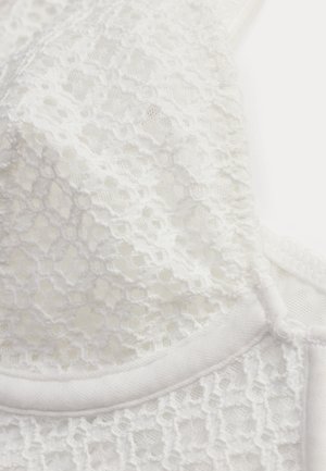 Tela de encaje blanco con patrones florales y bordes ondulados en una sección de primer plano de una prenda.