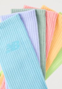 Στοίβα από πολύχρωμες ριγέ κάλτσες σε μπλε, λεβάντα, πράσινο, ροζ, πορτοκαλί και ανοιχτό πράσινο, τοποθετημένες σε μορφή βεντάλιας σε ανοιχτό φόντο.