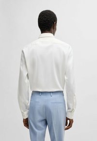 Camicia bianca a maniche lunghe con colletto classico, abbinata a pantaloni su misura azzurri chiari con due tasche posteriori. Tessuto con una superficie liscia.