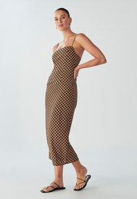 Hnedo-čierna midi šaty s potlačou, s priliehavým korzetom, tenkými ramienkami a rozšíreným spodným okrajom. Nosí sa s čiernymi plochými sandálmi.