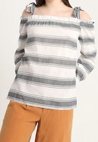 Vit off-the-shoulder blus med svarta ränder, volangkrage och knytband på axlarna. Lättviktsmaterial med en avslappnad passform.