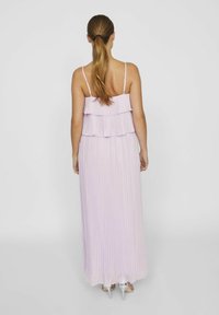 Robe maxi plissée lavande avec des détails en volants superposés et des fines bretelles. Elle présente un corsage ajusté et tombe au sol.