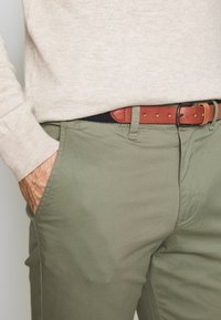 Kakifares chinos med en slät yta, med sidofickor och ett brunt läderbälte med en ljusbrun finish och synlig sömnad.