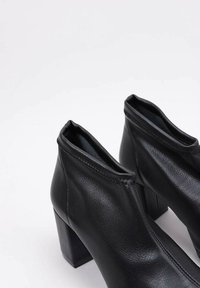 Black leather ankle boots with a square heel, minimalist design, smooth texture, and no visible hardware. Slightly elastic opening.