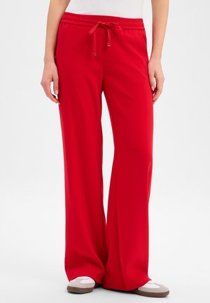 Frau trägt weite rote Hosen mit elastischem Bund und Kordelzug, kombiniert mit weißen und beigefarbenen Sneakers.