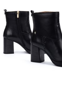 Botas de piel negras hasta el tobillo con un tacón grueso, cremalleras laterales y detalles de costura decorativa en el exterior.