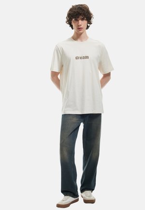 Hvid bomulds t-shirt med "dream" tekstdesign, parret med mørkeblå denim jeans og hvide sneakers med brune såler. Afbalanceret pasform, afslappet stil.