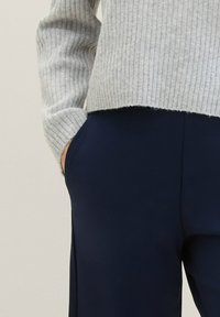 Grå ribbad tröja med en kortad fåll, tillsammans med marinblå byxor med sidofickor och ett slätt, texturerat tyg.