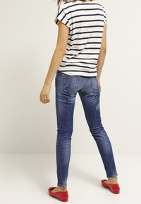 Top a rayas de manga corta en blanco y azul marino, combinado con jeans ajustados y desgastados azules con detalles en verde, y unas bailarinas rojas.