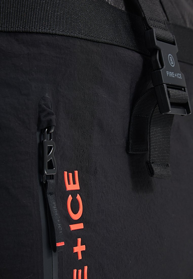 Schwarze Skijacke aus Stoff mit strukturiertem Oberflächen, ausgestattet mit einer Reißverschlusstasche und reflektierender orangefarbener "FIRE + ICE"-Markierung an der Seite. Verstellbare Gurtbeschläge.