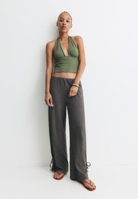 Maslinasto zeleni halter top s dubokim izrezom, uparen s labavim, teksturiranim tamnosivim hlačama s bočnim trakama i smešnim japankama.