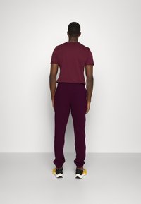 Weinrotes T-Shirt mit kurzen Ärmeln und tiefpurpurfarbene Jogginghose, die einen lockeren Schnitt und einen elastischen Bund hat. Kombiniert mit schwarzen und gelben Turnschuhen.