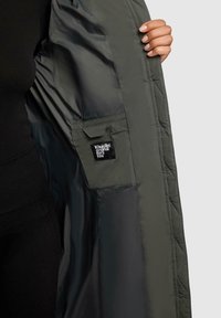 Gequilted groene jas met een gladde voering, voorzien van een zak en een label dat op de binnennaad is gestikt.