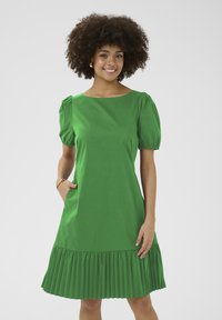 Zelena obleka z kvadratnim izrezom, napihnjenimi rokavi in nabrano obrobo. Narejena iz lahko tkanine z gladko teksturo.