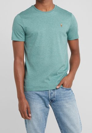 T-shirt turquoise en coton avec des manches courtes, col rond et petit logo brodé sur la poitrine gauche. Assorti à un jean bleu clair.