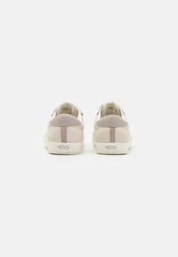 Baskets en suède beige avec un contre-talons en cuir gris lisse, une semelle en caoutchouc blanche et un marquage discret près du talon.