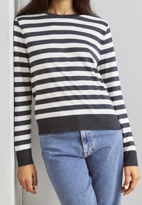 Gestreiftes langärmliges Oberteil in Marineblau und Weiß aus Baumwollgemisch, mit Rundhalsausschnitt und geripptem Saum, kombiniert mit hellblauen Jeans.