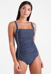 Maillot de bain une pièce marine à pois avec encolure carrée, bretelles épaisses, côtés froncés et détails en piping blanc sur le devant.