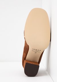 Chaussure à talon haut en daim marron avec un talon bloc, présentant une semelle lisse et une étiquette de marque embossée. Taille 37, fabriquée au Portugal.