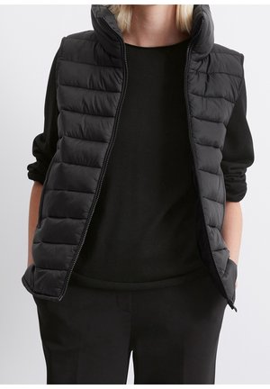 Schwarze Pufferweste mit hohem Kragen, kapuziniertem Design und Reißverschluss, über einem schwarzen Langarmshirt getragen.