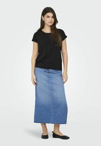 T-shirt nero a maniche corte abbinato a una maxi gonna in denim azzurro chiaro con orlo sfilacciato e zip frontale. Ballerine nere completano l'outfit.