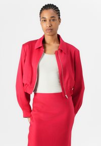 Red bomber jacket with a zip front, ribbed cuffs, and a relaxed fit, paired with a fitted light gray tank top and matching red skirt.