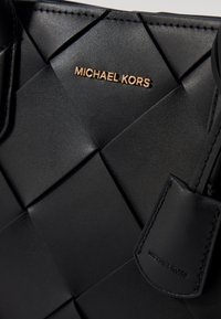 Sort vævet lædertaske med et guld logo og et mærkat med mærkenavnet. Glat tekstur med et struktureret design og robuste håndtag.