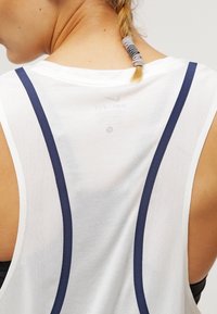Witte sportieve tanktop met marineblauwe accentbandjes, een meshstructuur en een ronde halslijn, ontworpen voor comfort en ademend vermogen.