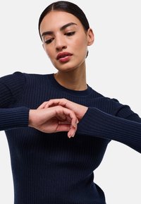 Pull en tricot côtelé bleu marine avec des longues manches et un col rond ; présente une surface texturée et une silhouette ajustée.