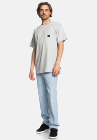 Grå kortærmet t-shirt med lomme, kombineret med lyseblå jeans og sorte sneakers. Minimalistisk design med en afslappet pasform.