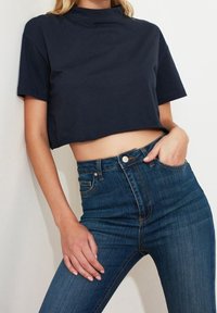 Marinblå kortärmad t-shirt med hög halsringning, kombinerad med mörkblå högmidjade jeans. Slät bomullstextur.