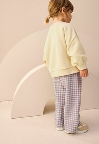 Jasnożółty, oversize'owy sweatshirt, spodnie w kratę w niebieskim, brązowym i białym kolorze oraz wielokolorowe sneakersy. Gładka tekstura, casualowy design.