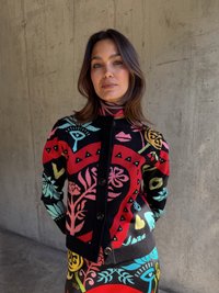 Pletený cardigan so živým viacfarebným kvetinovým vzorom na čiernom pozadí, s kruhovým výstrihom a predným zapínaním na gombíky.