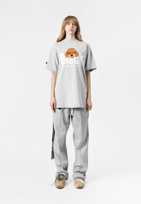 Camiseta oversized gris claro con un gráfico texturizado de un perro marrón y texto en negrita "Black", combinada con pantalones gris claro y zapatillas beige.