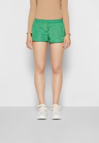 Calções atléticos verdes com uma cintura elástica, feitos de tecido leve, com bolsos laterais e um pequeno logótipo na parte da frente.