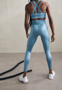 Soutien-gorge de sport bleu clair avec des bretelles croisées, assorti à un legging taille haute. Tissu lisse et extensible avec des chaussures de sport blanches.
