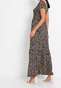 Černé květinové maxi šaty s krátkým rukávem, s tiered spodním dílem a malými bílými a růžovými květinami. Nosené s béžovými podpatky.