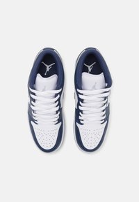 Fehér és sötétkék bőrsneaker perforált orr-résszel, fehér fűzővel és Jumpman logóval a nyelvén, sima felülettel és alacsony szárú kialakítással.